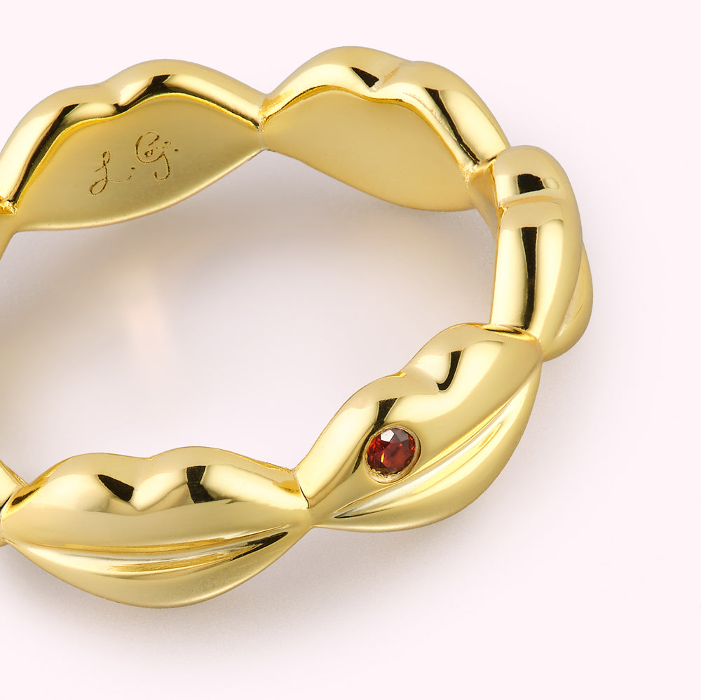 Close up of gold lip ring with inset ruby stone and engraved brand logo inside the band.