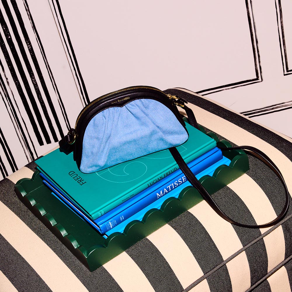 Denim and leather crossbody bag on top of a pile of books on a striped chair.