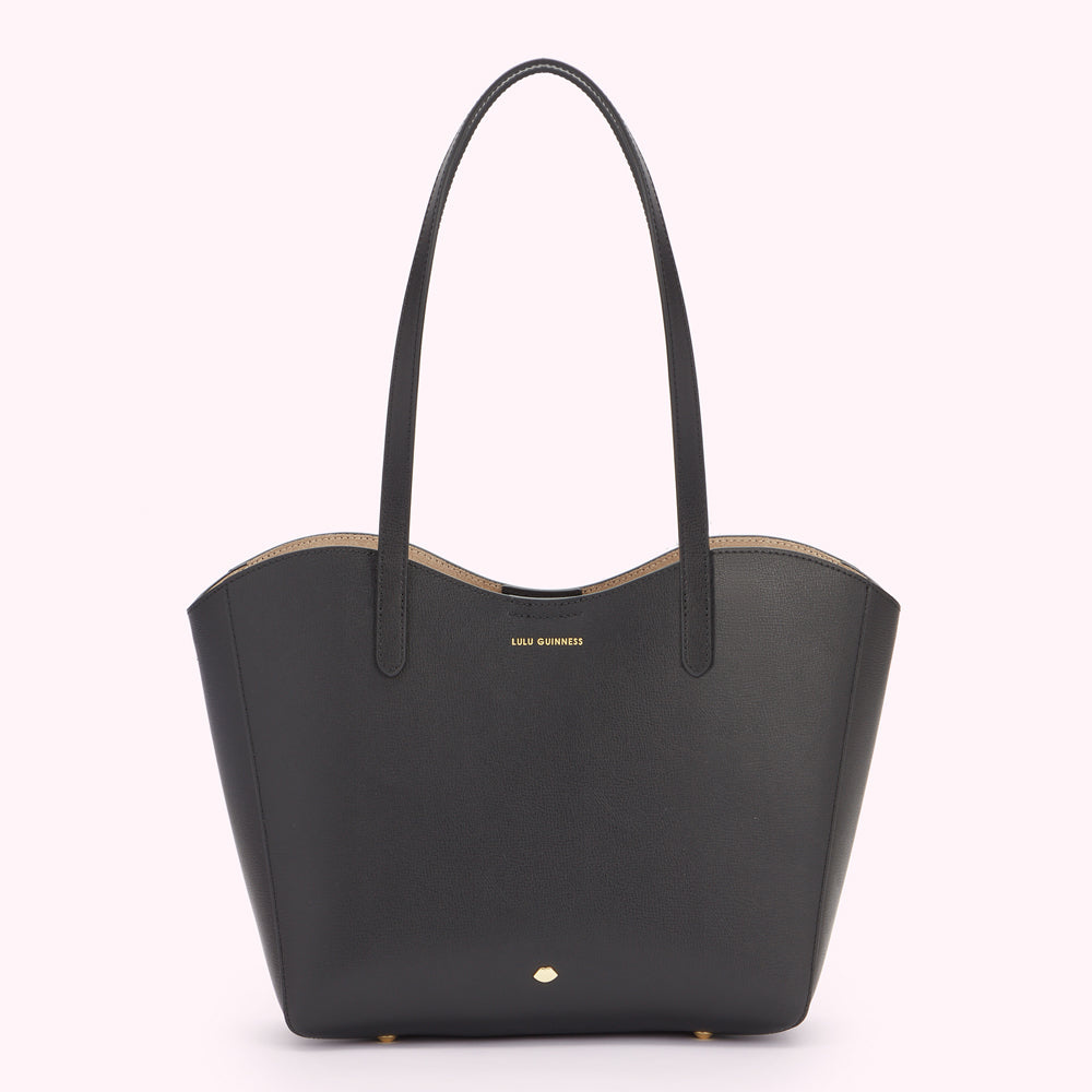 Front image of a black leather tote bag with a curved front edge. Showing a gold metal lip pin at the bottom and gold foil Lulu Guinness logo at the top. 