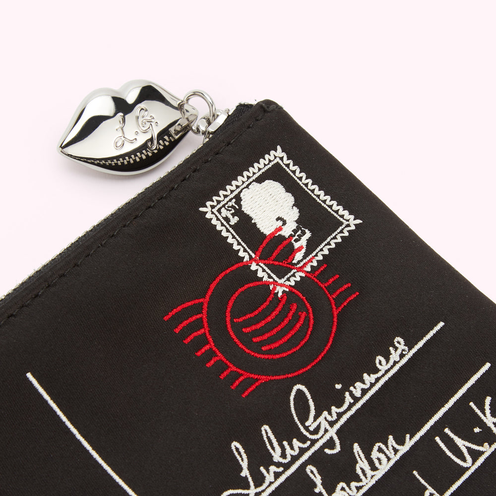 Close-up of a black zip pouch with a silver lip-shaped zipper pull and red and white embroidered postage stamp details.