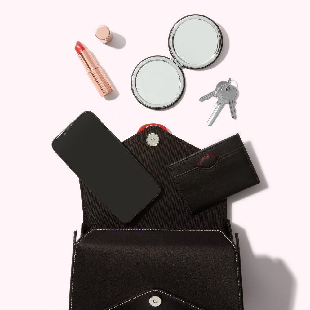 Open black purse with smartphone, lipstick, compact mirror, and keys on a white background.