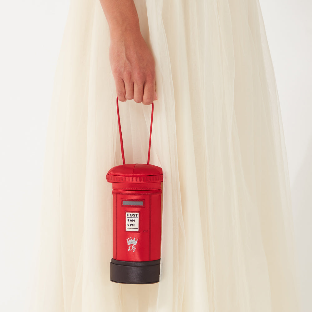 A woman in a white dress holds a small red handbag shaped like a British post box.