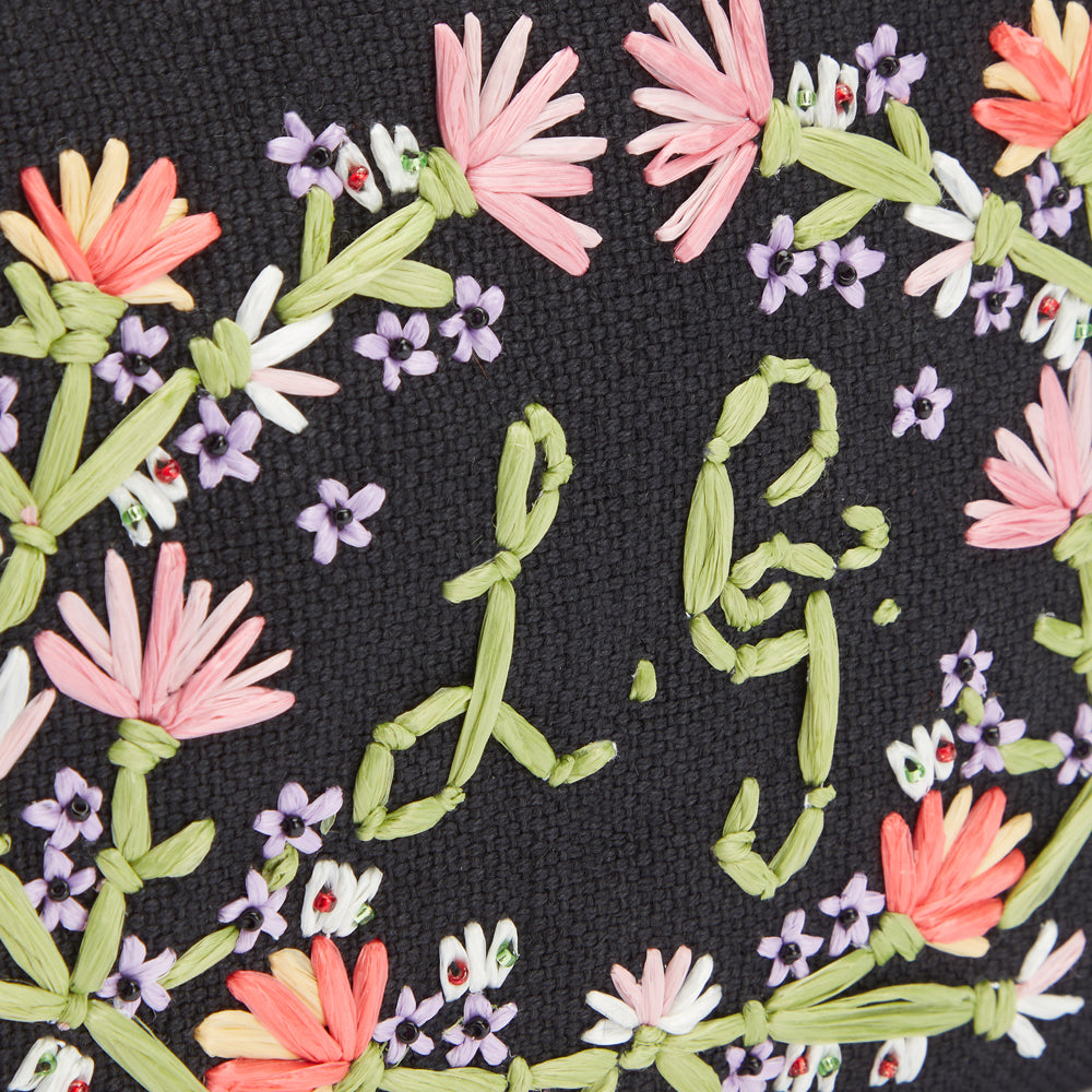 Close up image of pastel floral embroidery on a black canvas pouch with embroidered L.G. monogram.