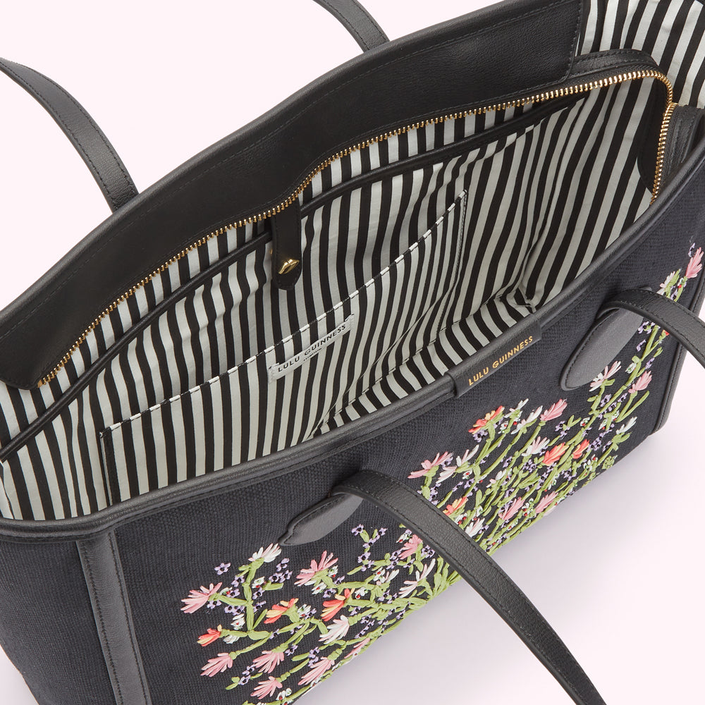 Inside image of black canvas and leather tote bag with pastel floral embroidery, showing the black and white striped lining and revealing a inside slip pocket and laptop pocket.