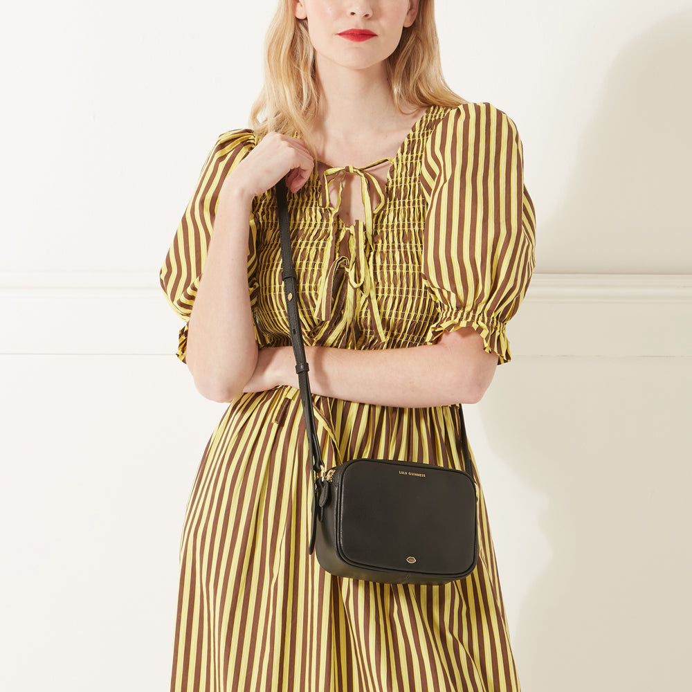 Model in a striped dress wearing a black leather crossbody bag.