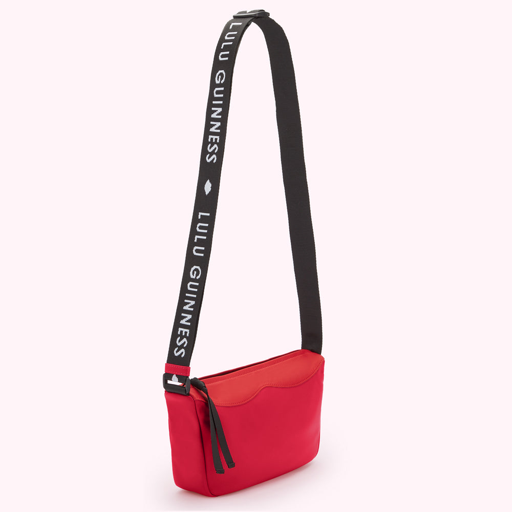 Red Lulu Guinness nylon crossbody bag with a black shoulder strap that says "Lulu Guinness."