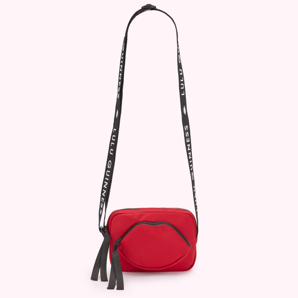 Red crossbody bag with a lip-shaped detail and a black strap with white "Lulu Guinness" lettering.