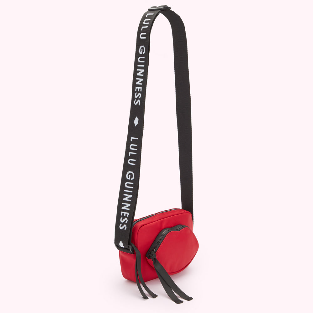 Red crossbody bag with a lip-shaped detail and black strap featuring repeating "Lulu Guinness" branding.