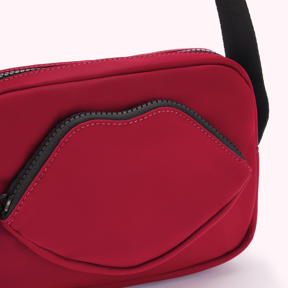 Close-up of a crimson red crossbody bag with a lip-shaped zipper pocket.
