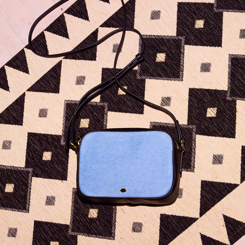 A denim and black leather crossbody bag laying on a geometric rug.