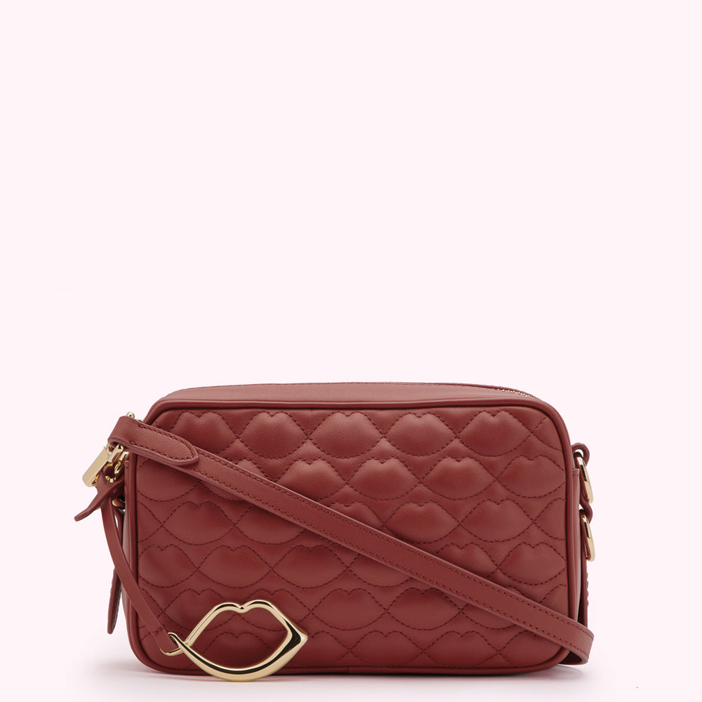 A rust-coloured quilted crossbody bag with a gold lip-shaped accent.
