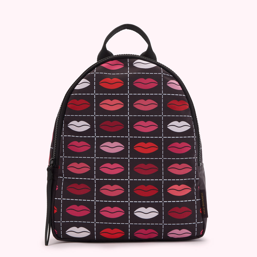 Black mini backpack with a repeating pattern of lips in various shades of red and pink on a dark background.