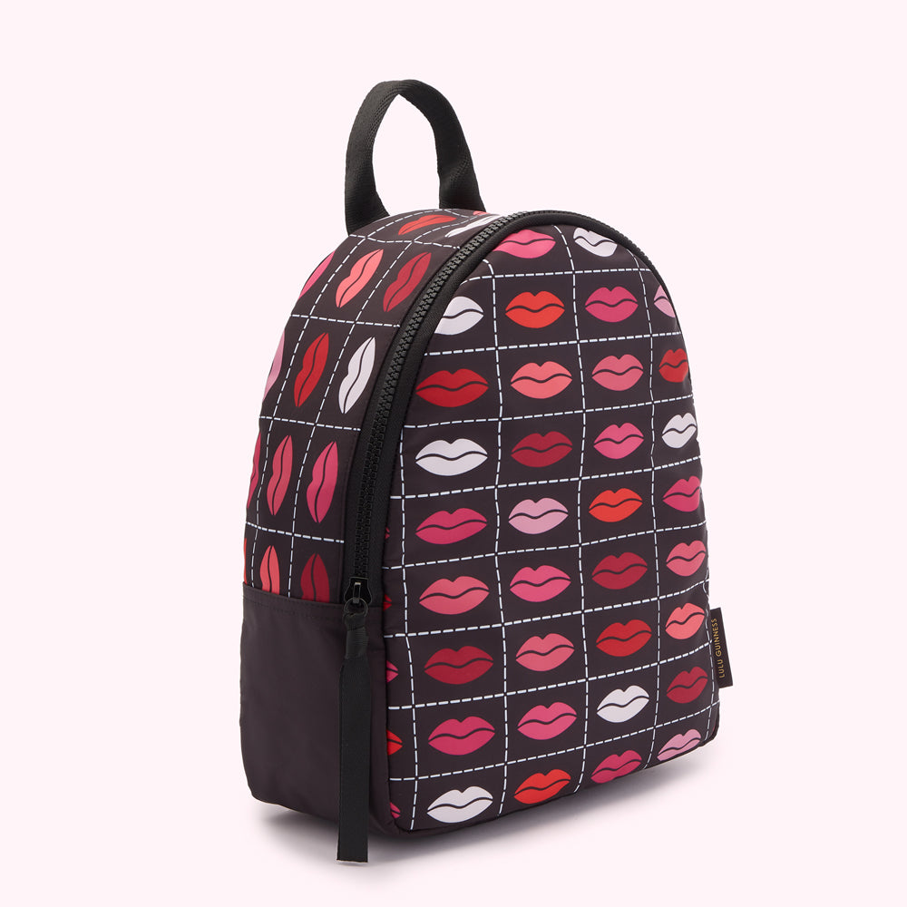 Black backpack with a repeating pattern of lips in various shades of pink and red on a white grid.