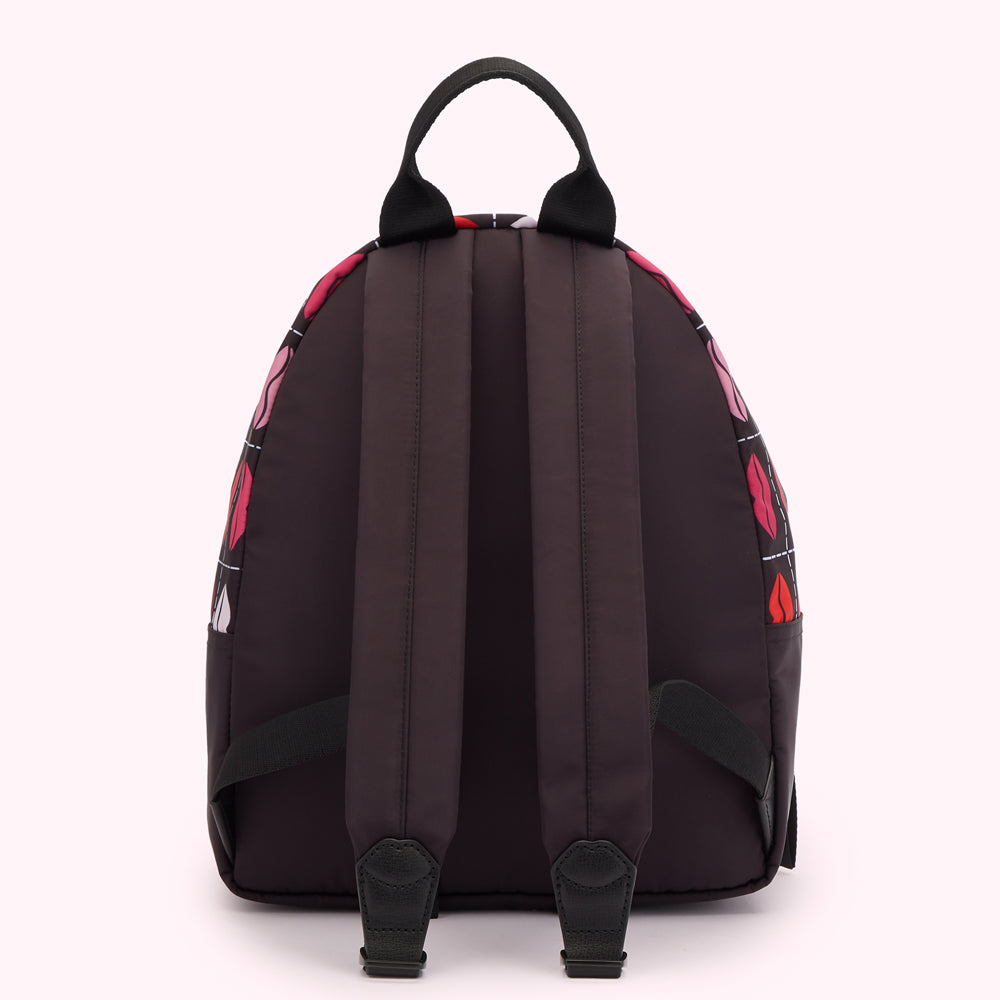 Dark purple backpack with a pattern of pink and red lips on a white background. The backpack is shown from the back.
