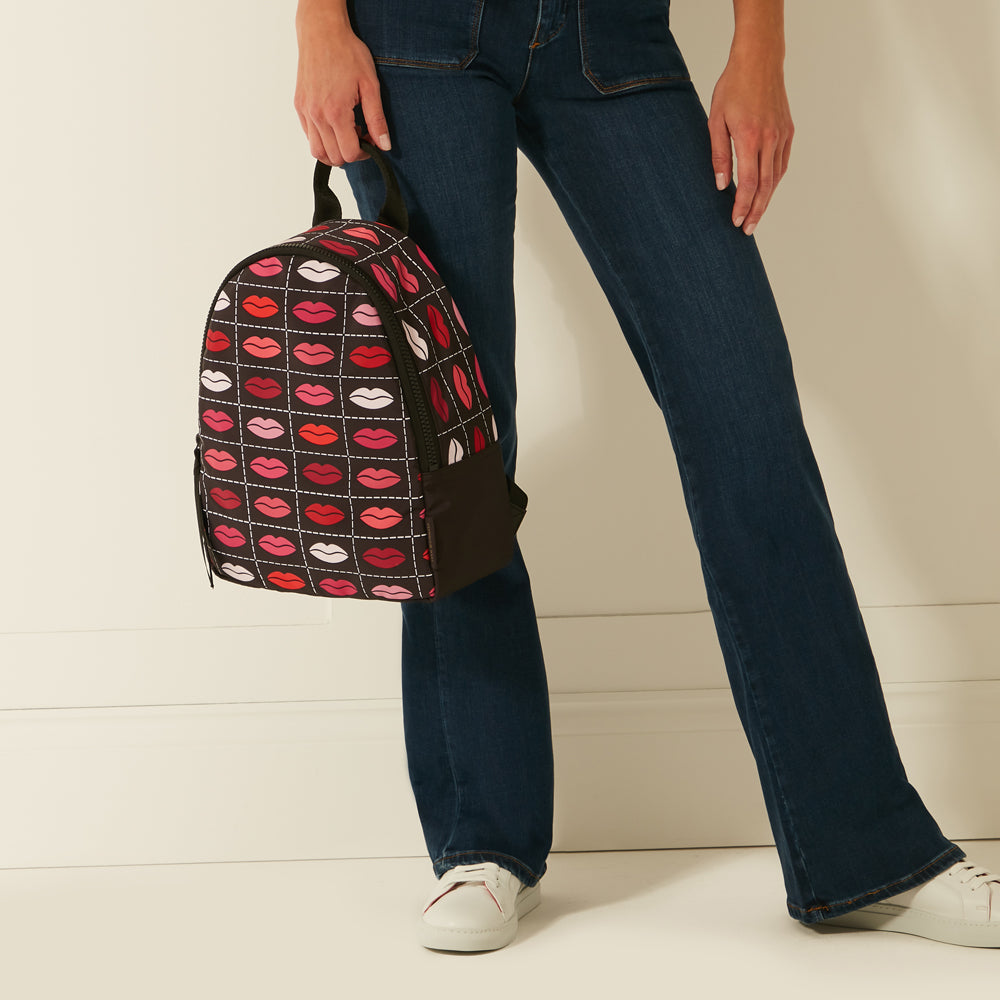 Person holding a black backpack with a red lips pattern against a white background.