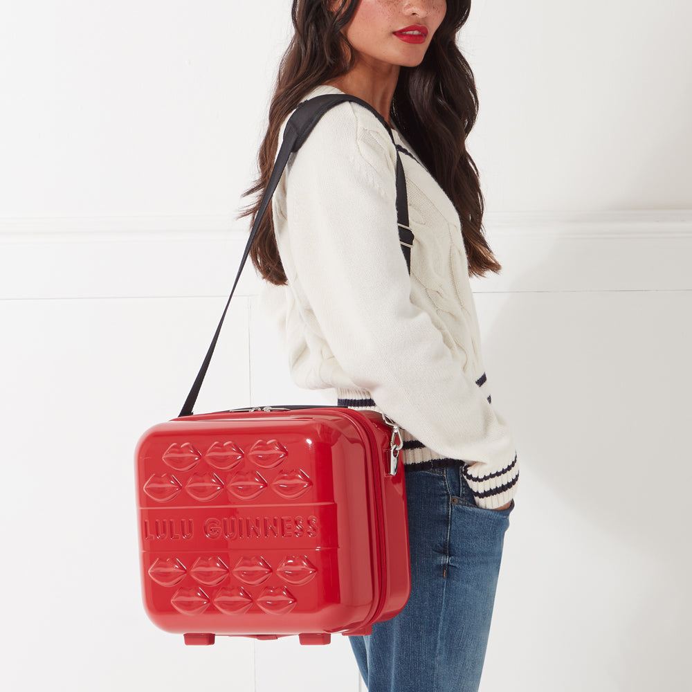 Red Lulu Guinness Lips cosmetic case with black shoulder strap worn by a woman.
