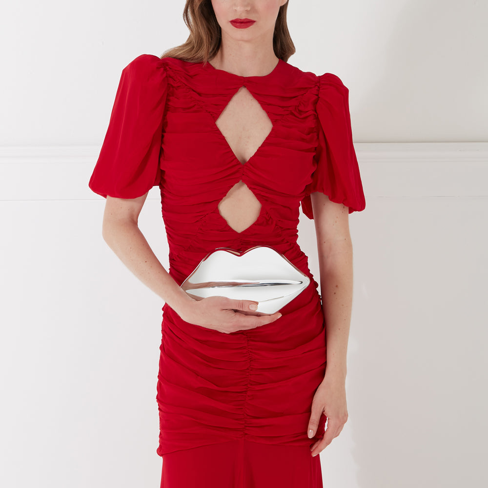 Woman in a red dress holding a silver lip-shaped clutch.
