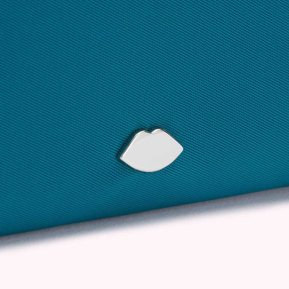 Close-up of a teal fabric surface with a silver lip-shaped emblem.
