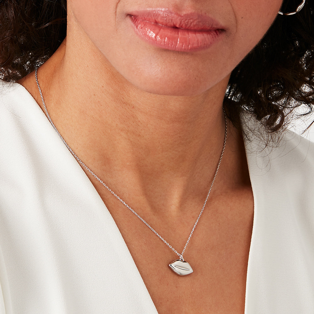 Close-up of a woman wearing a silver necklace with a lip-shaped pendant against a white background.
