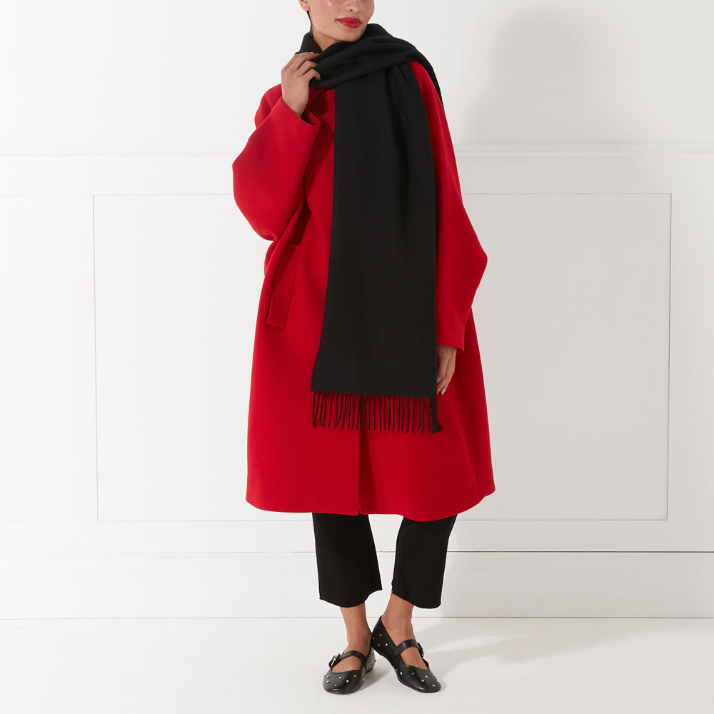 Woman in red coat and black scarf and shoes against a white background.
