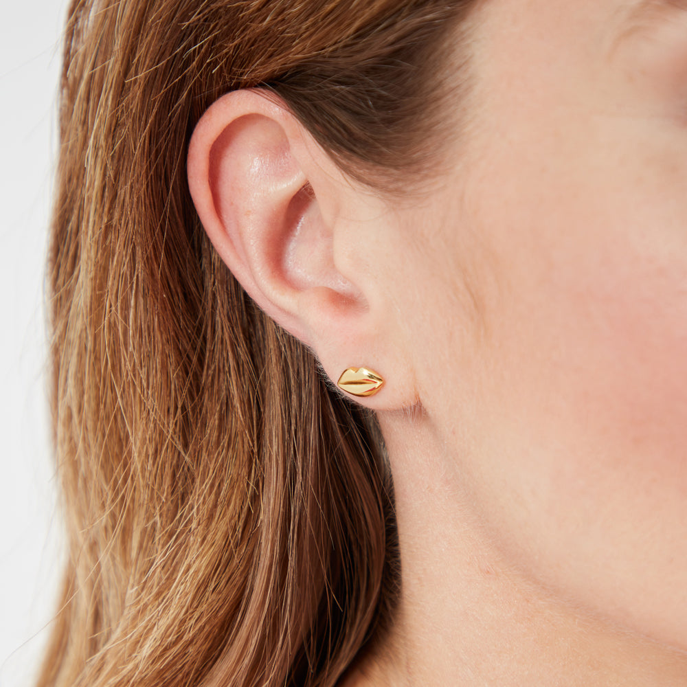 Close-up of a woman's ear with gold lip-shaped stud earrings.
