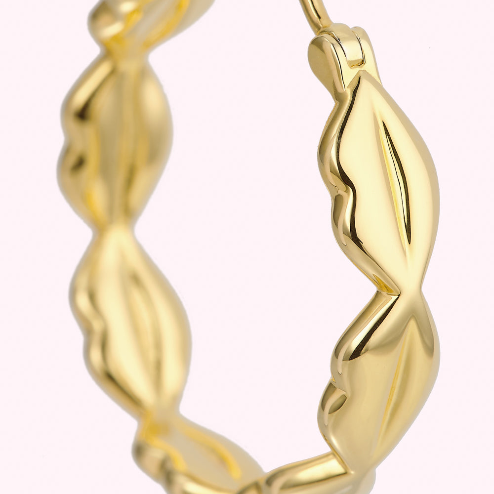 Close-up of a gold hoop earring with a leaf-like design.