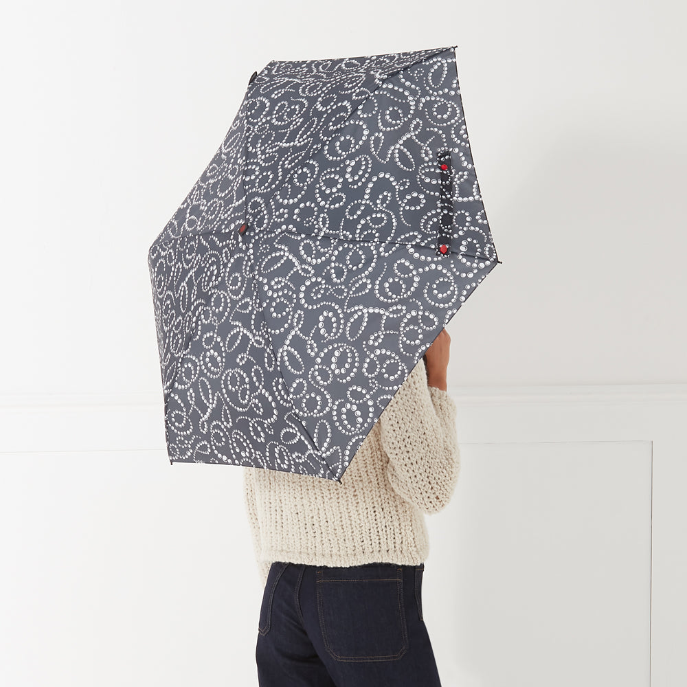 A person holds a dark grey umbrella with a white pearl pattern behind their back against a white background.