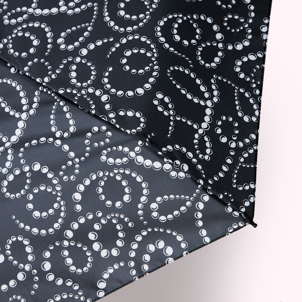 Close-up of a dark grey umbrella with a pattern of white pearl-like circles arranged in swirling designs.