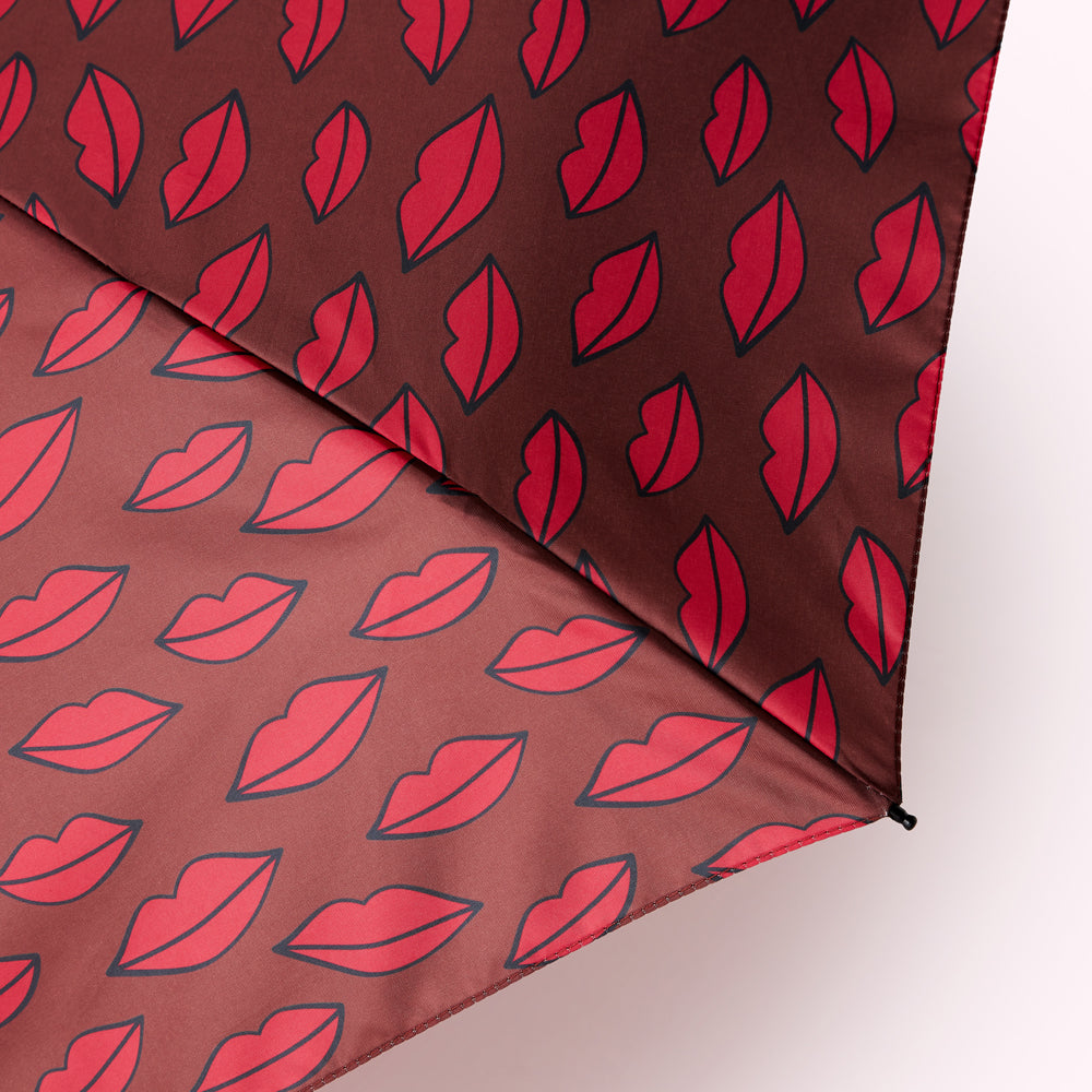 Close-up of a maroon umbrella with a repeating pattern of red lips.
