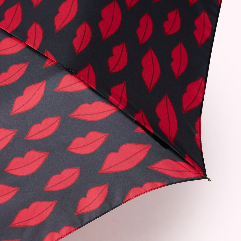 Close-up of a partially opened umbrella with a two-toned design featuring red lips on a dark grey and black background.
