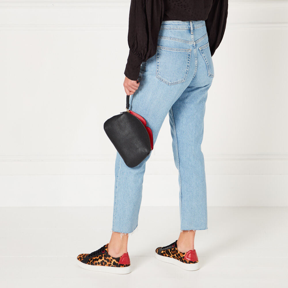 Woman in light blue jeans and leopard print sneakers holding a black and red purse.
