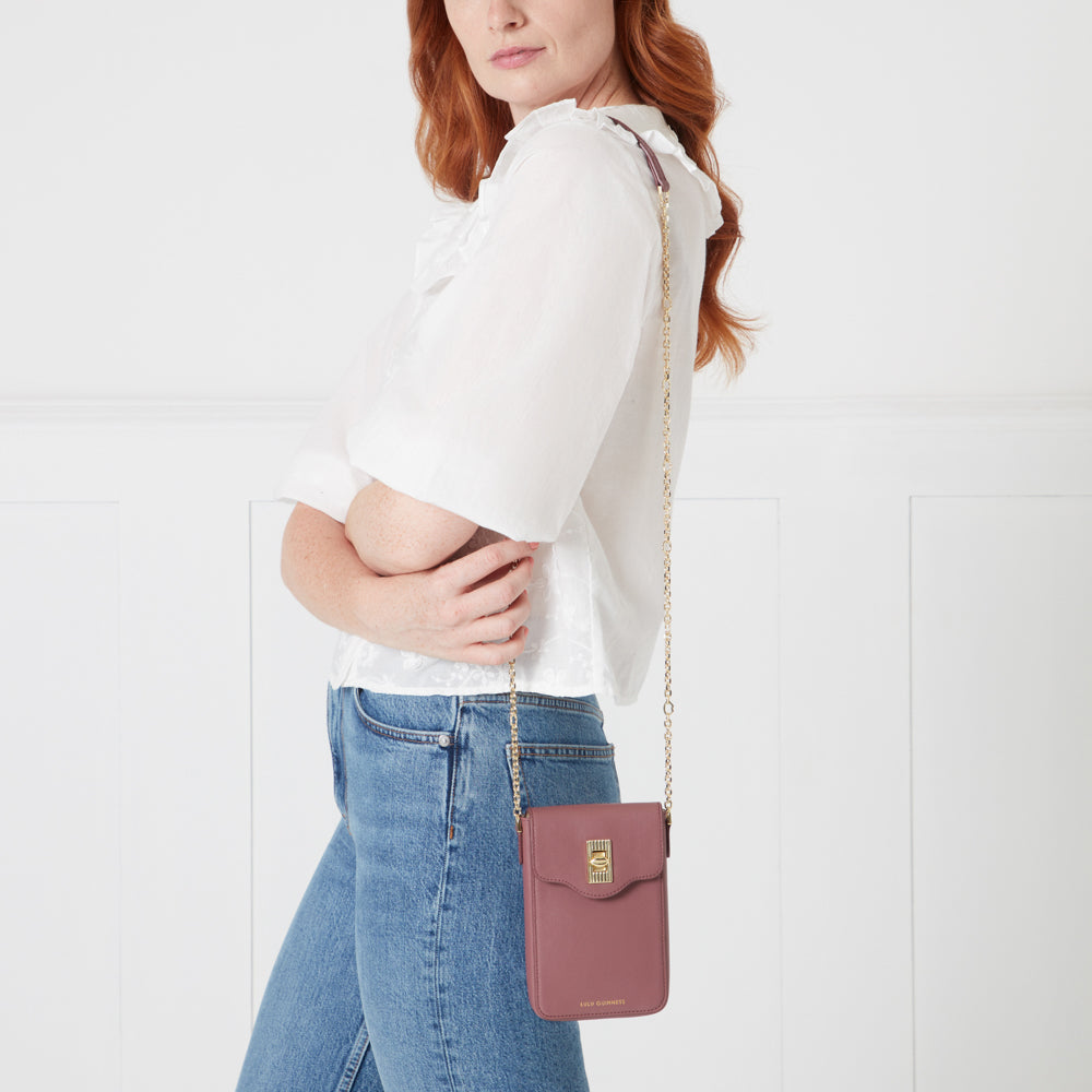 Woman with long red hair wearing a white blouse and blue jeans, a dusty rose coloured crossbody bag with gold chain strap.