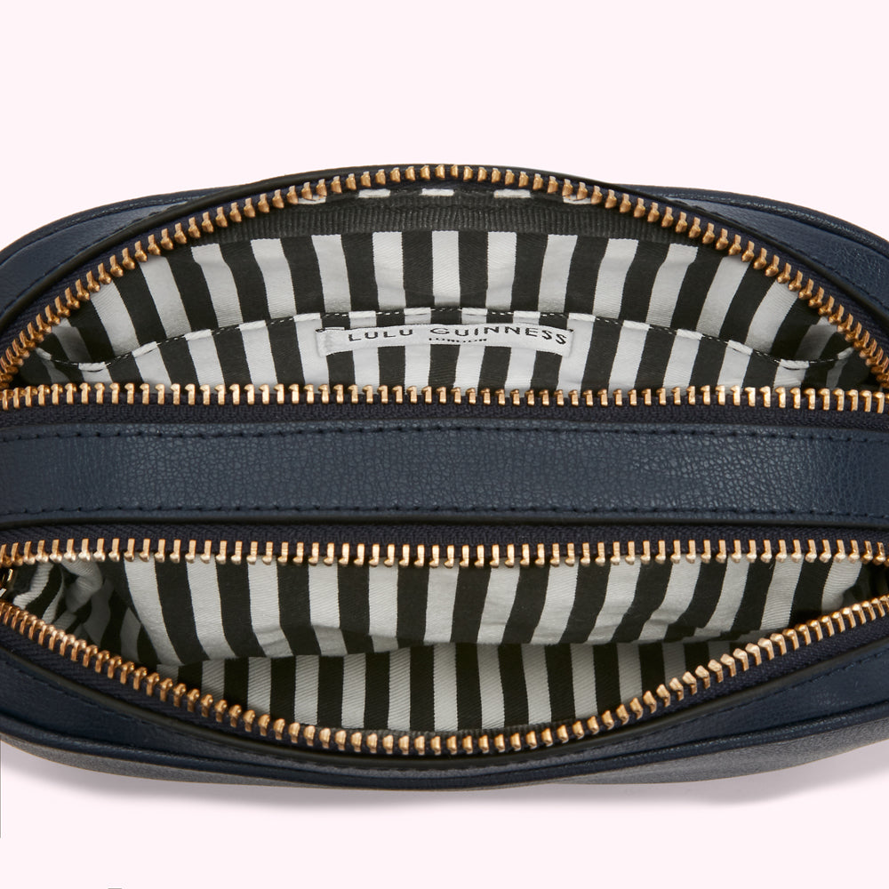 Inside of a navy blue Lulu Guinness crossbody bag with gold zippers and a black and white striped interior.