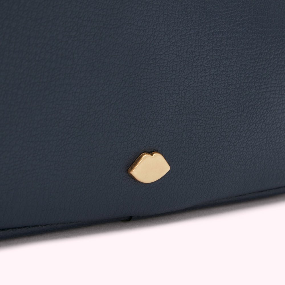 Close-up of a dark blue textured purse with a gold lip-shaped emblem.
