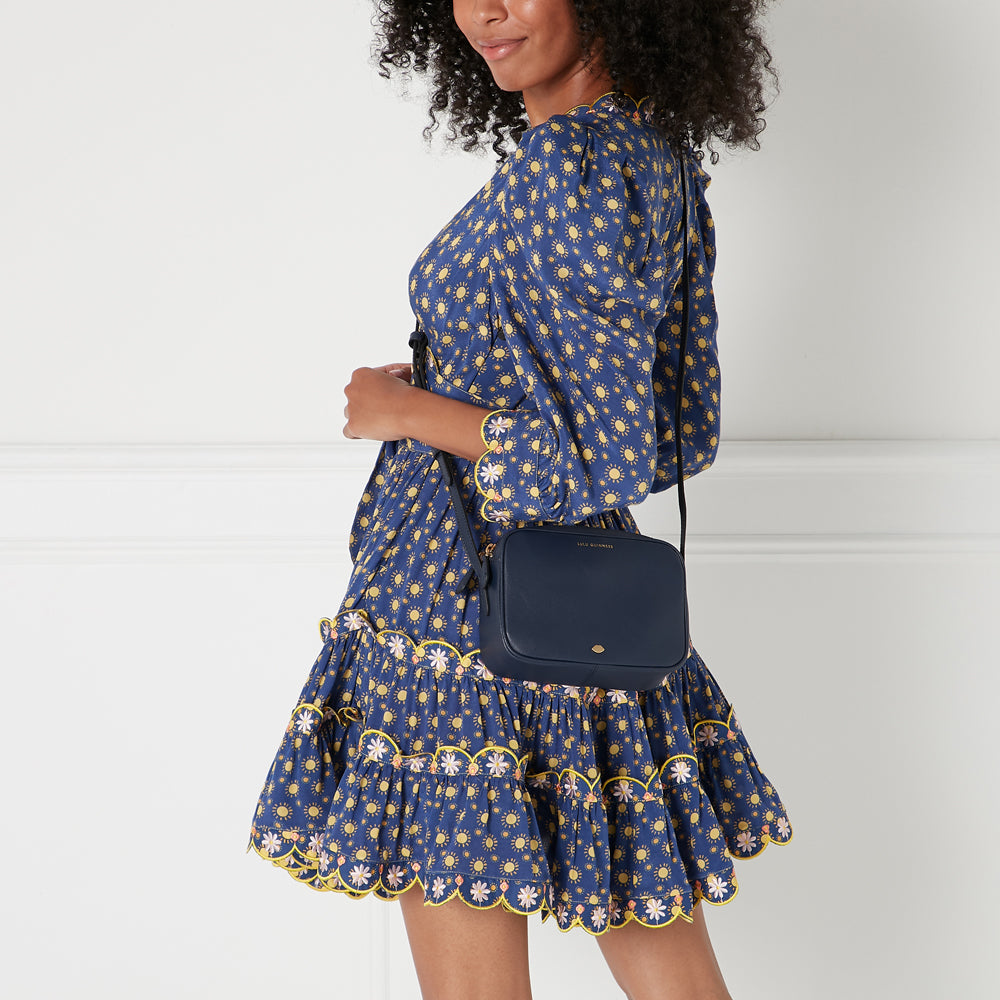 Woman in blue floral dress with navy crossbody bag.
