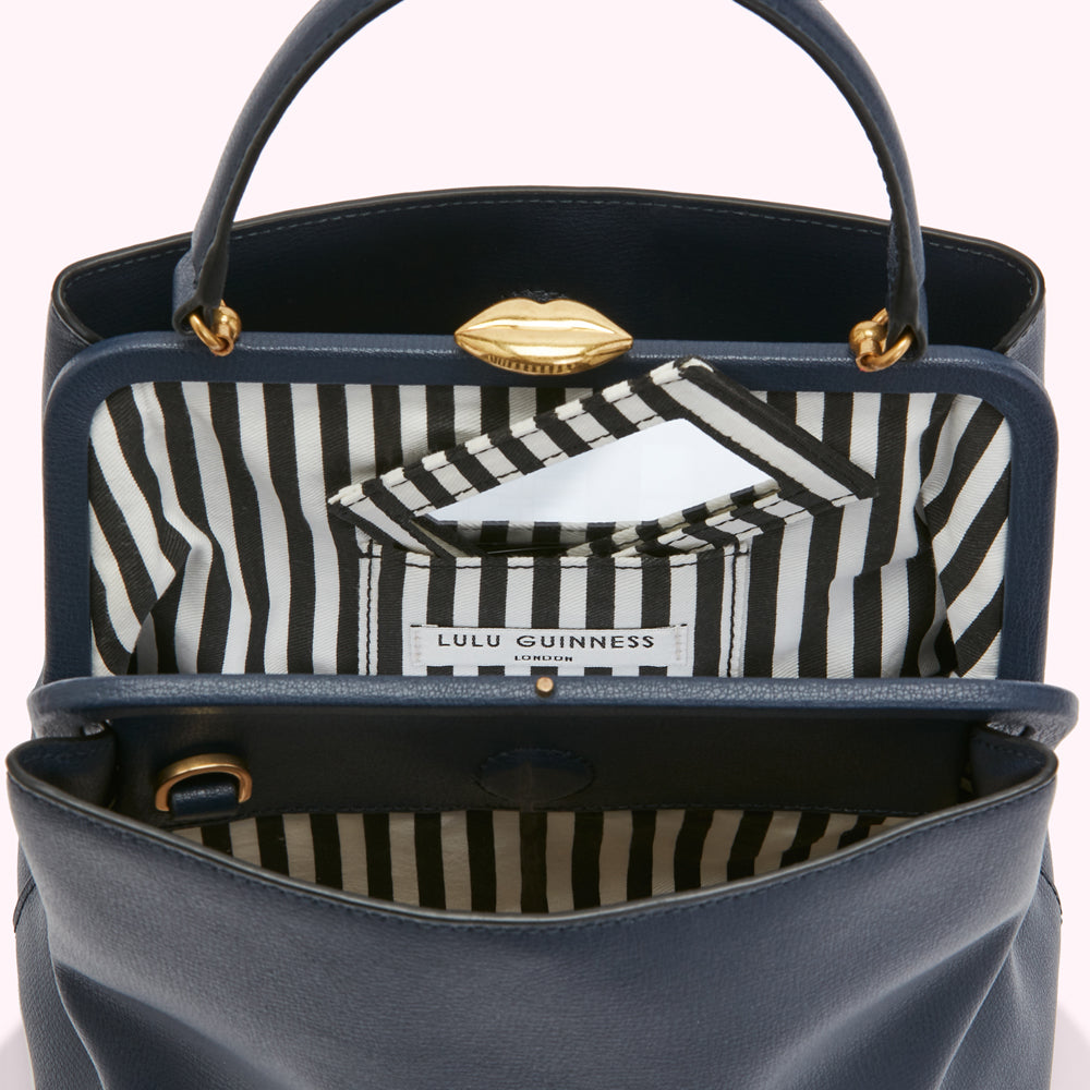 Interior view of a navy blue Lulu Guinness handbag with a black and white striped lining and gold clasp.
