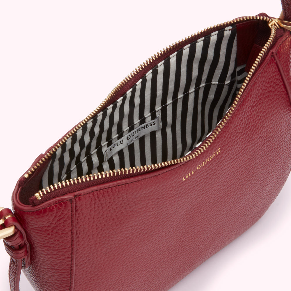 Interior of a burgundy Lulu Guinness crossbody bag with black and white striped lining.