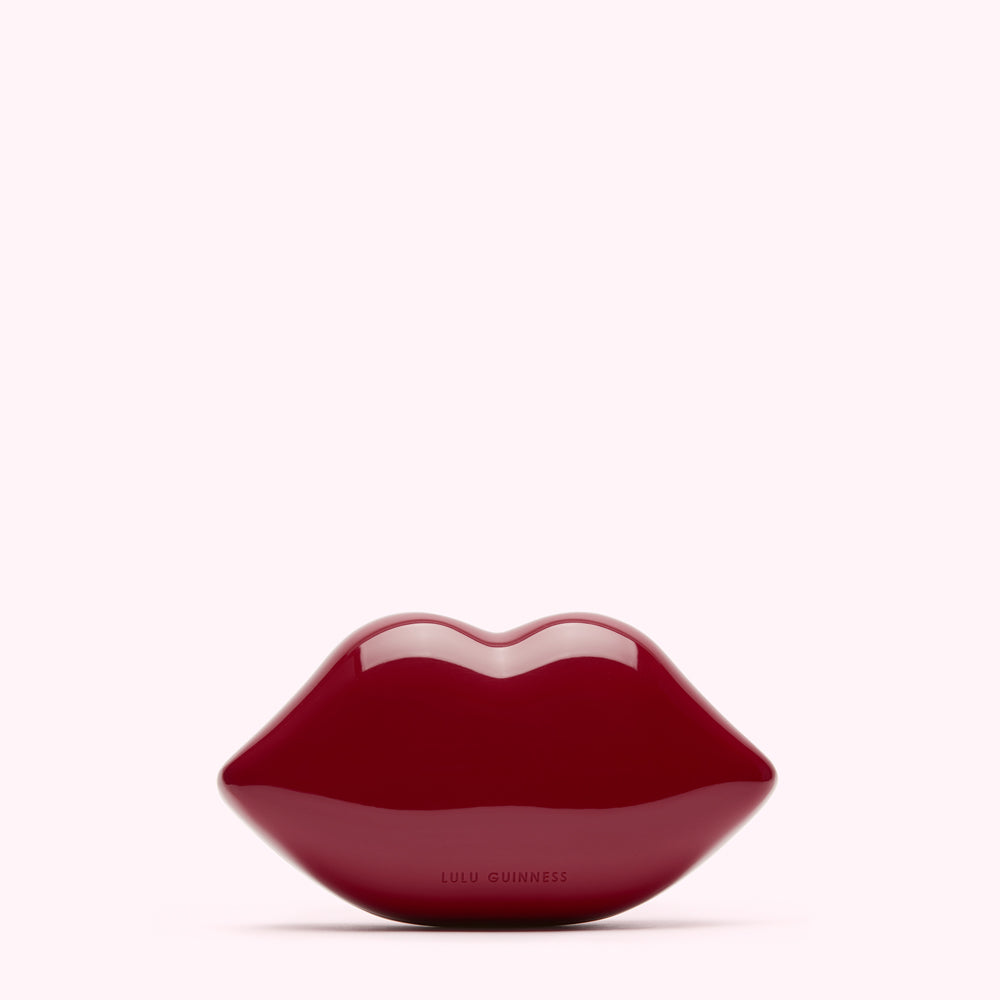 A dark red Lulu Guinness lips clutch bag against a white background.
