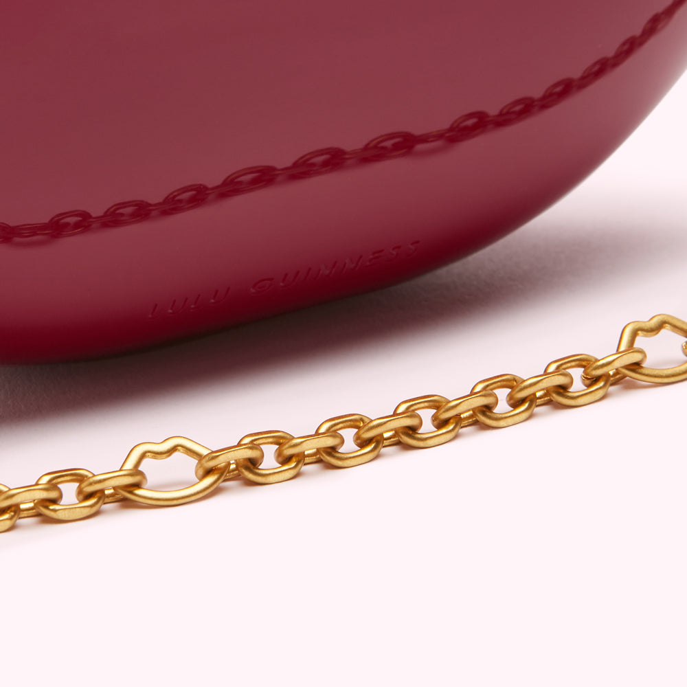 Close-up of a burgundy Lulu Guinness handbag with a gold chain strap, showing the brand's logo embossed on the bag.
