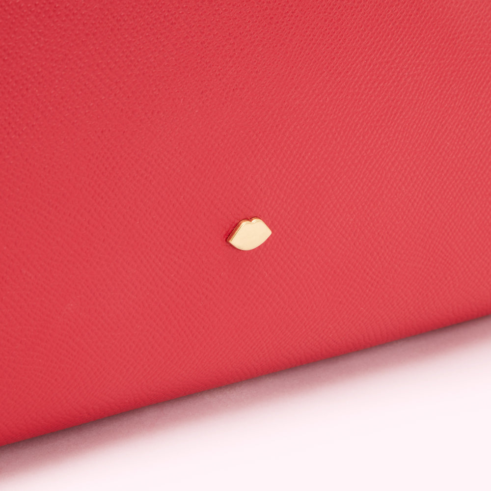 Close-up of a red leather item with a small gold lip emblem.
