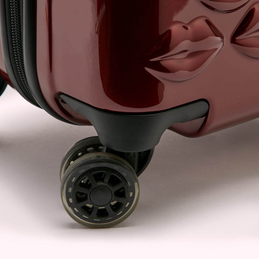 Close-up of a dark red suitcase wheel, showcasing its design and the suitcase's unique lip-shaped design.
