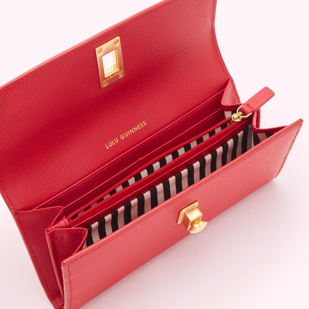 Open red Lulu Guinness wallet with gold clasp and black and white striped interior.
