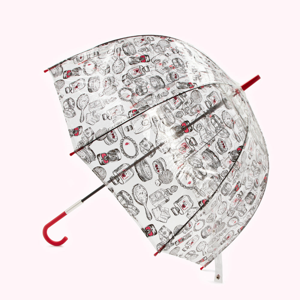 Clear umbrella with a black and red pattern of beauty products printed on it. The handle is red.
